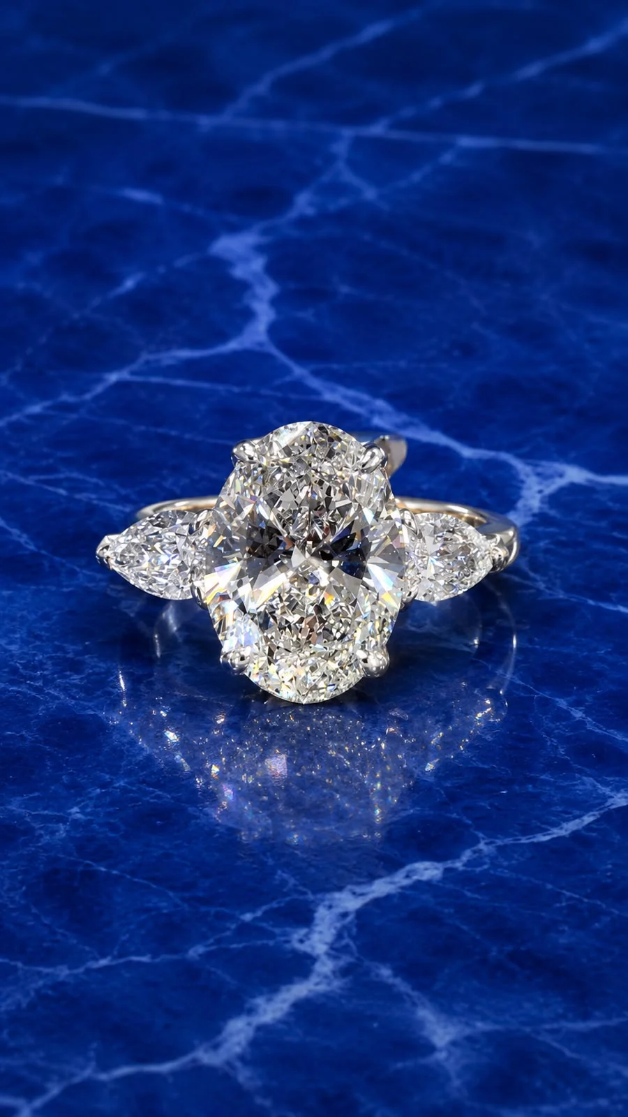 Three stone engagement ring with an oval cut lab grown diamond center and pear side diamonds